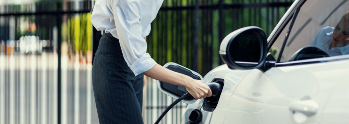 Closeup progressive suit-clad businesswoman with her electric vehicle recharge her car on public charging station in modern city with power cable plug and renewable energy-powered electric vehicle.